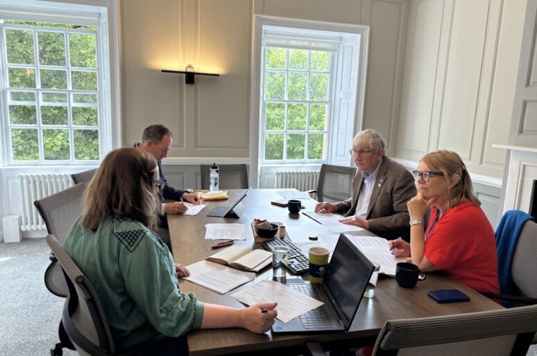 Four people in a meeting room, sat around a table looking at Bath Building Society Community Award application documents
