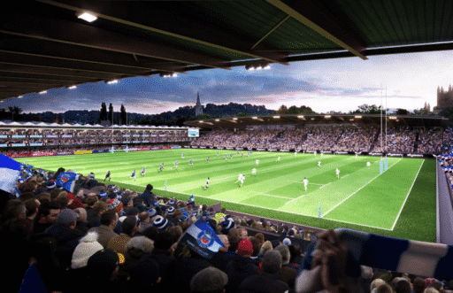 CGI of Bath Rugby’s proposed new 18,000-seat stadium at The Rec, showing a packed crowd watching a rugby match from the covered stands, with the pitch, posts, and Bath skyline in the background.