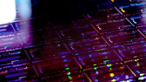 Detailed close‑up of a thin‑film lithium niobate chip array, highlighting precision‑etched circuitry and colourful light reflections across the wafer surface.