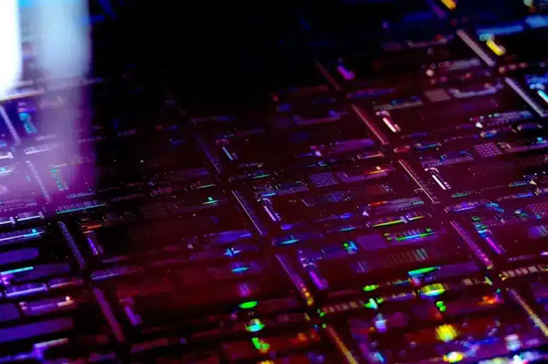 Detailed close‑up of a thin‑film lithium niobate chip array, highlighting precision‑etched circuitry and colourful light reflections across the wafer surface.