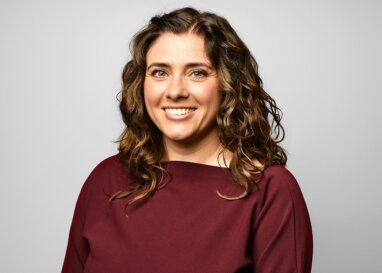 Rachael Abbott wearing a deep burgundy top with long wavy hair.